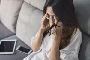 Young woman take off her glasses and sitting on sofa